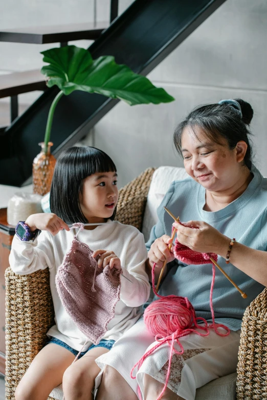 a woman sitting on a chair next to a little girl, pexels contest winner, arts and crafts movement, yarn, singapore, sweater, thumbnail