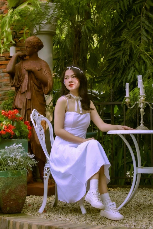 a woman in a white dress sitting at a table, a statue, inspired by Kim Du-ryang, pexels contest winner, sitting on chair, garden, vietnamese woman, low quality photo