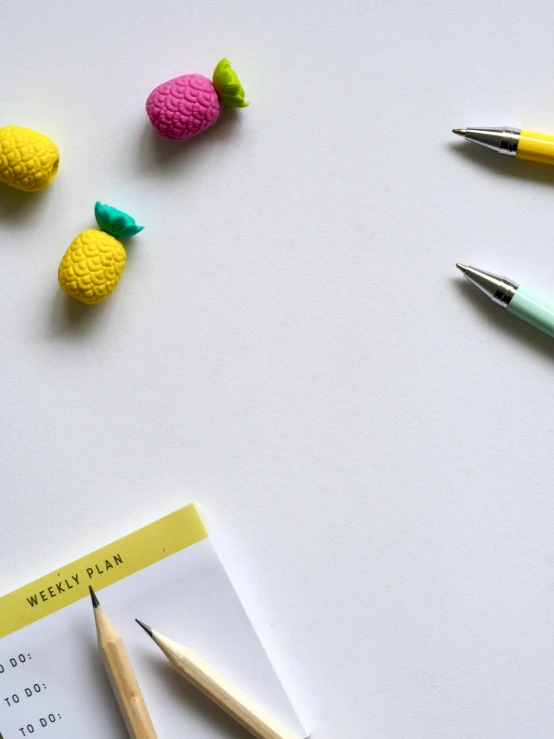 a notepad sitting on top of a table next to a bunch of crocheted pineapples, by Robbie Trevino, pexels contest winner, visual art, pencils, neon accents, miniatures, set against a white background