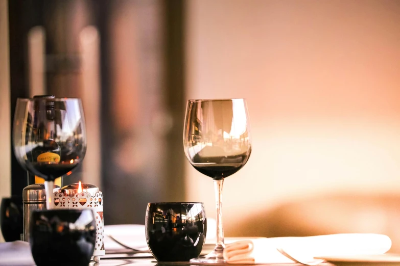 a couple of wine glasses sitting on top of a table, pexels contest winner, black and red scheme, warm light, place setting, in a row