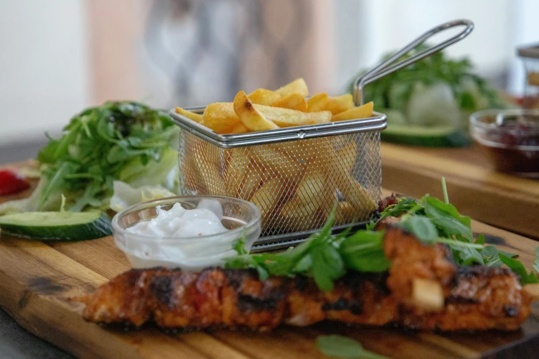 a wooden cutting board topped with a basket of food, coke and chips on table, greens), kebab, up close shot