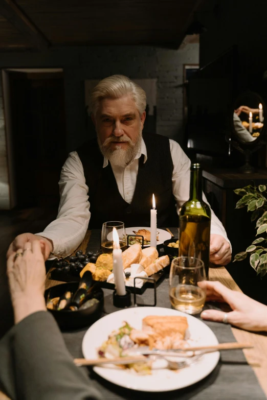 a group of people sitting around a dinner table, greybeard, candle lit, dark grey haired man, [ theatrical ]