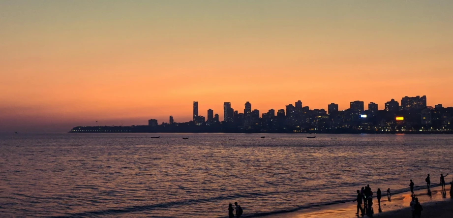 a group of people standing on top of a beach next to the ocean, pexels contest winner, romanticism, streets of mumbai, twilight skyline, orange skies, vancouver