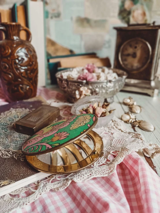 a book sitting on top of a table next to a clock, a still life, inspired by Lucy Madox Brown, trending on unsplash, arts and crafts movement, vintage makeup, with a mirror, green and pink fabric, made of intricate metal and wood