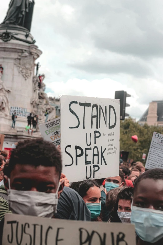 a group of people holding signs in front of a statue, by Emma Andijewska, trending on pexels, ears are listening, france, black man, with violence