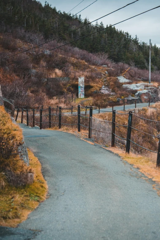 a sign that is on the side of a road, by Roar Kjernstad, unsplash, detailed fences and stone walls, downhill landscape, fall season, 🚿🗝📝