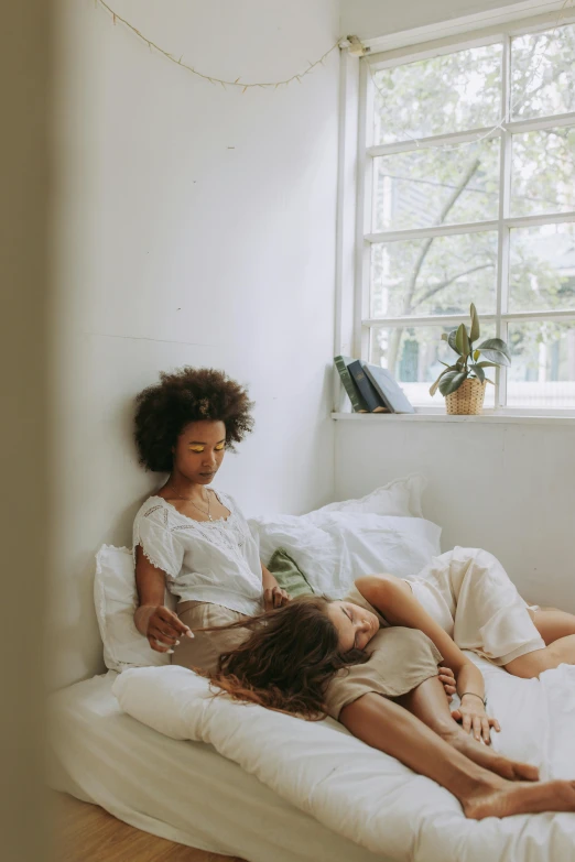 a couple of kids laying on top of a bed, by Jessie Algie, pexels contest winner, romanticism, young women, in white room, afternoon hangout, woman holding another woman