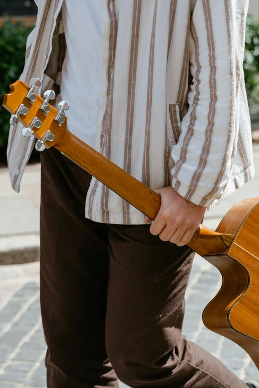 a man walking down the street holding a guitar, inspired by John McLaughlin, unsplash, renaissance, brown clothes, zoomed in, summer day, handcrafted