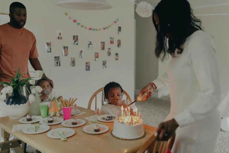 a woman blowing out candles on a birthday cake, by Arabella Rankin, pexels contest winner, dark-skinned, husband wife and son, full body image, on a white table