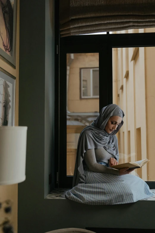 a woman sitting on a window sill reading a book, inspired by Maryam Hashemi, hurufiyya, wearing a grey robe, commercially ready, sitting across the room, student