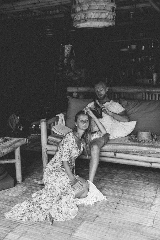 a black and white photo of a woman sitting on a couch, a black and white photo, tumblr, happening, barabas miklos and hollosy simon, in africa, in a cabin, barefoot in sandals