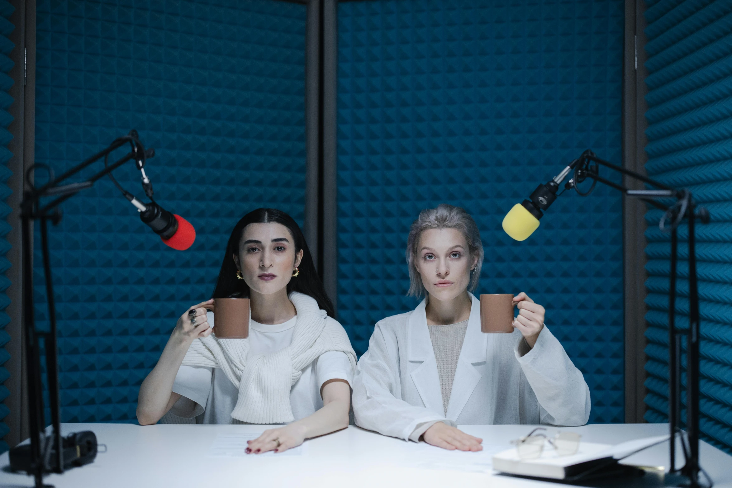 two women sitting at a table in front of microphones, an album cover, by Emma Andijewska, shutterstock, lie detector test, alessio albi, h3h3, two cups of coffee