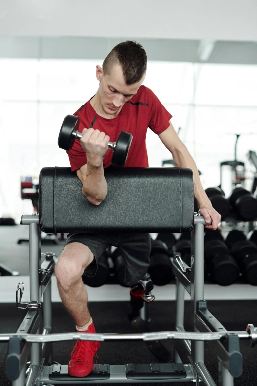 a man sitting on top of a bench in a gym, a colorized photo, pexels contest winner, prosthetics, square, thin young male, red and grey only