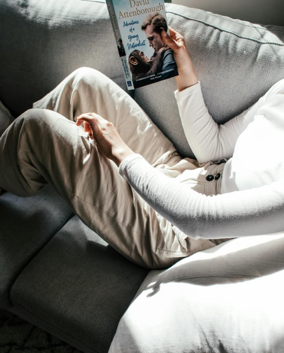 a woman sitting on a couch reading a book, inspired by Sarah Lucas, pexels contest winner, baggy pants, wearing a white sweater, high angle, lara croft relaxing