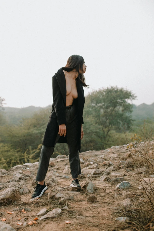 a woman standing on top of a rocky hill, trending on pexels, black leather bra, wearing black overcoat, provocative indian, trending on r/techwearclothing