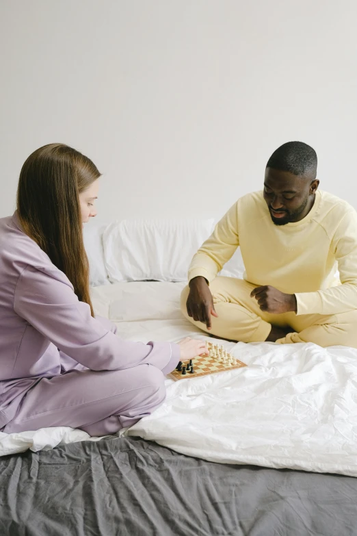 a man and a woman playing chess on a bed, wearing a purple sweatsuit, muted colors with minimalism, in a gold suit, wearing nanotech honeycomb robe