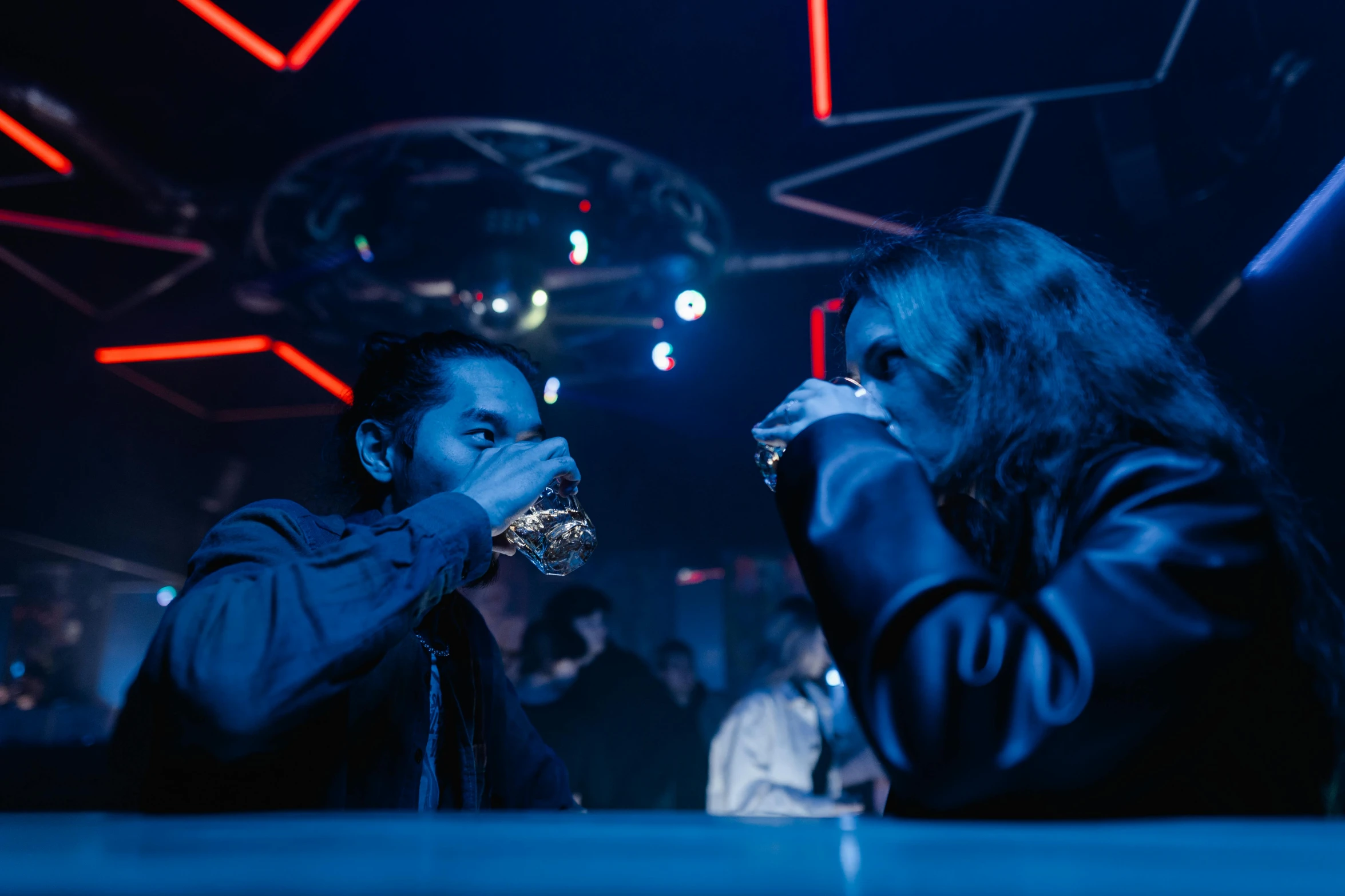 a couple of people that are sitting at a table, by Adam Marczyński, nightclub, cinematic still, ap, laser