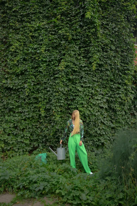 a woman that is standing in the grass, inspired by Ren Hang, trending on pexels, overgrown ivy plants, green corduroy pants, watering can, with long blond hair