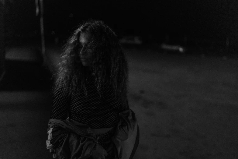 a black and white photo of a woman with long hair, unsplash, outdoors at night, curly haired, gloomy lighting, on the ground