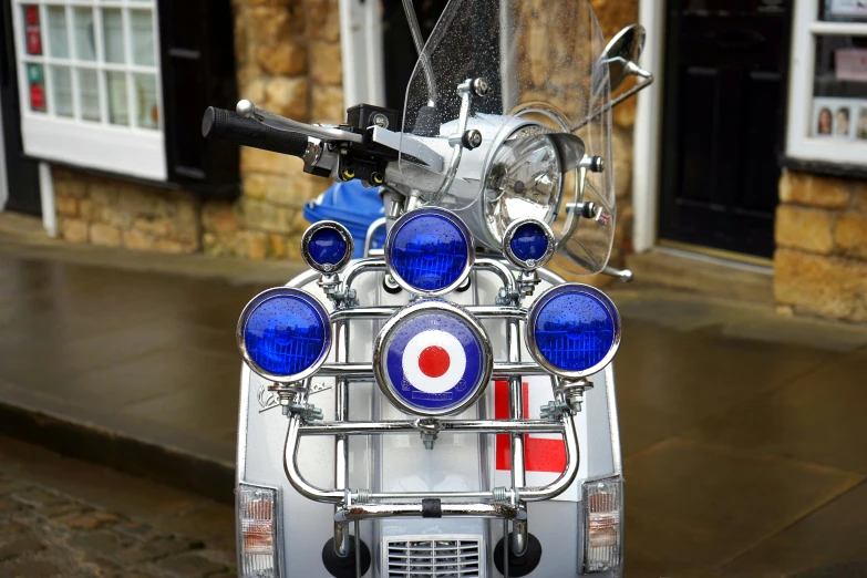 a motor scooter parked in front of a building, blue and silver, yorkshire, tail lights, replicas