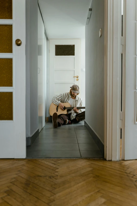 a man sitting on the floor playing a guitar, by Sebastian Spreng, pexels contest winner, apartment hallway, doorway, plain background, reuniting