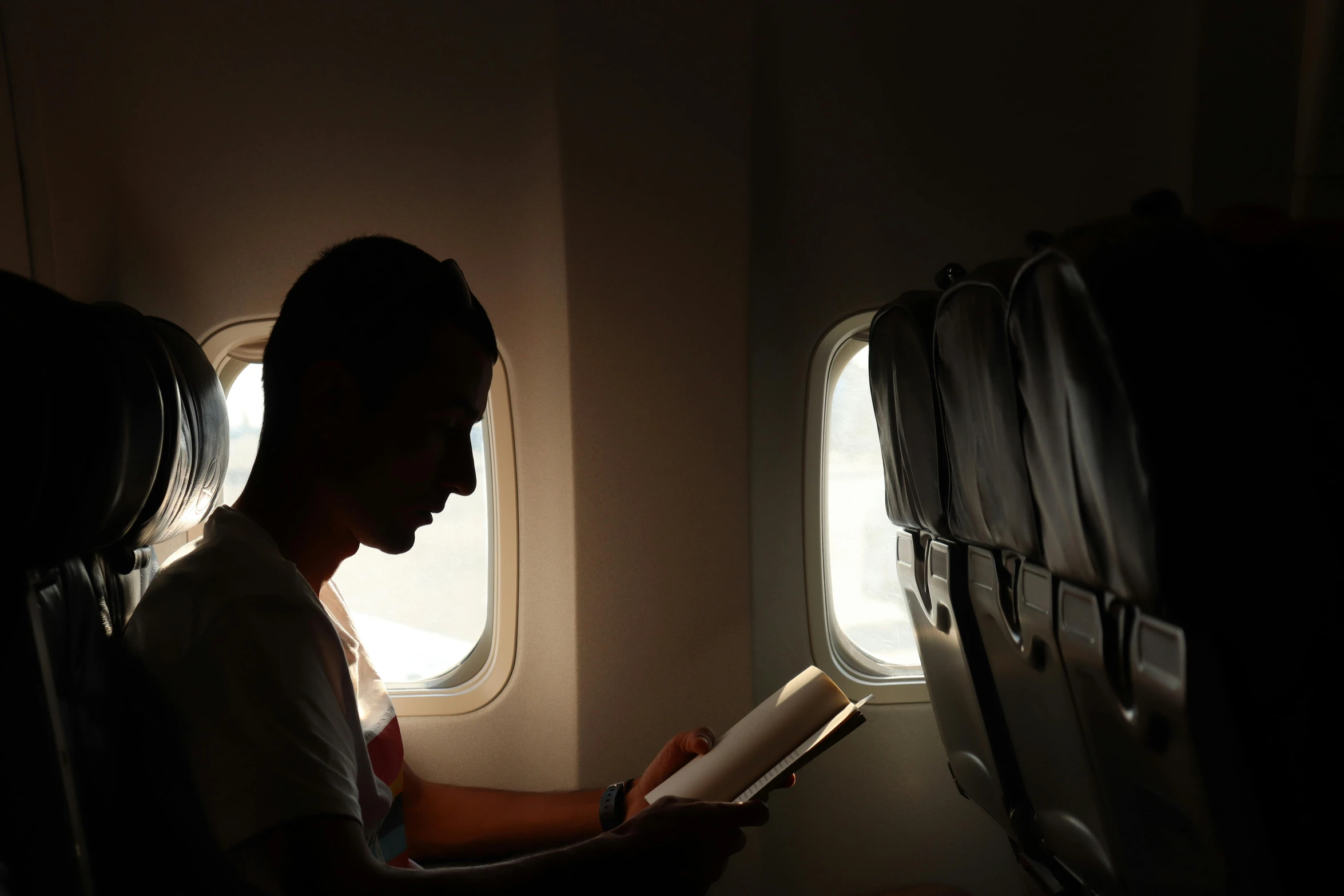 a man sitting in an airplane reading a book, by Jessie Algie, pexels contest winner, happening, back light, light stubble, ilustration, multiple stories