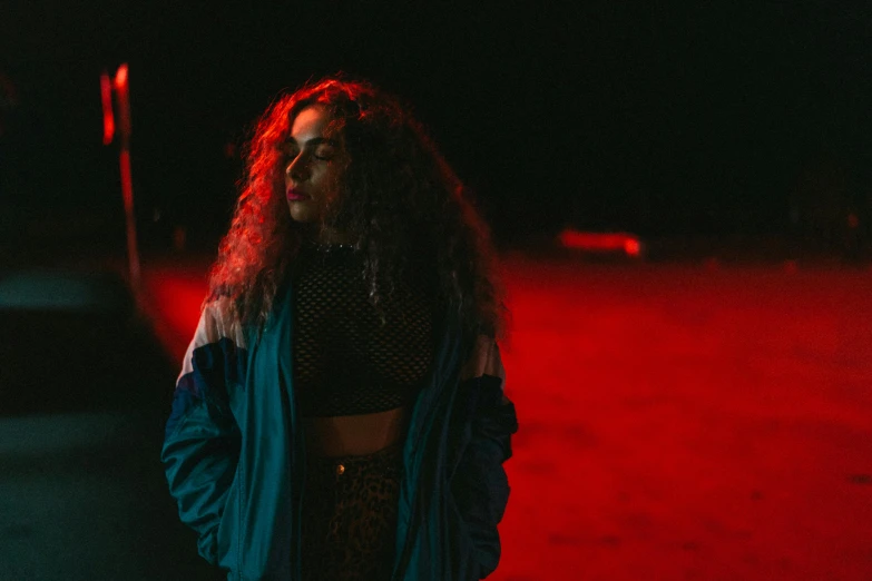 a woman standing in the middle of a street at night, an album cover, inspired by Elsa Bleda, pexels contest winner, antipodeans, red curly hair, cool red jacket, blue and red lights, performing a music video