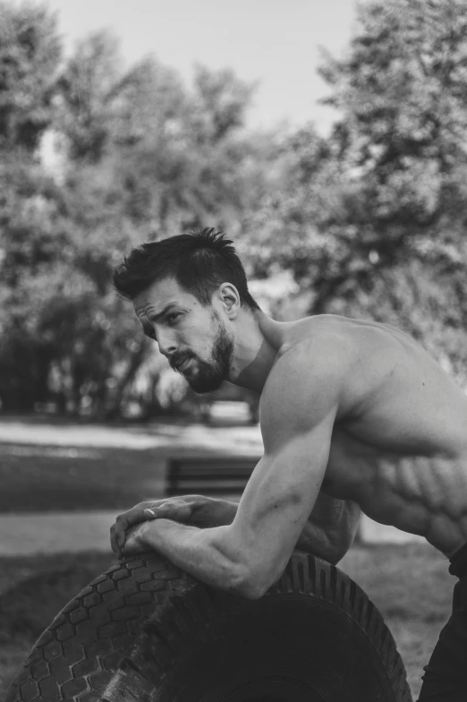 a shirtless man leaning on a tire, a black and white photo, sitting on a park bench, goatee, instagram picture, 30 year old man :: athletic
