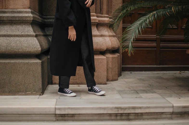 a man in a black coat standing in front of a building, by Emma Andijewska, pexels contest winner, wearing white sneakers, wearing a black robe, close-up on legs, androgynous person