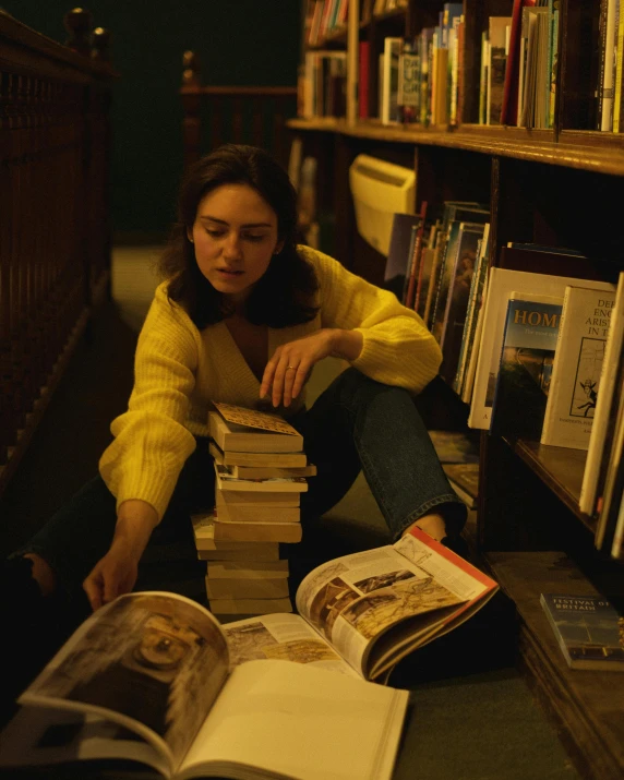 a woman sitting on the floor next to a pile of books, inspired by Nan Goldin, trending on unsplash, happening, yellow clothes, low quality photo, oona chaplin, 70s photo