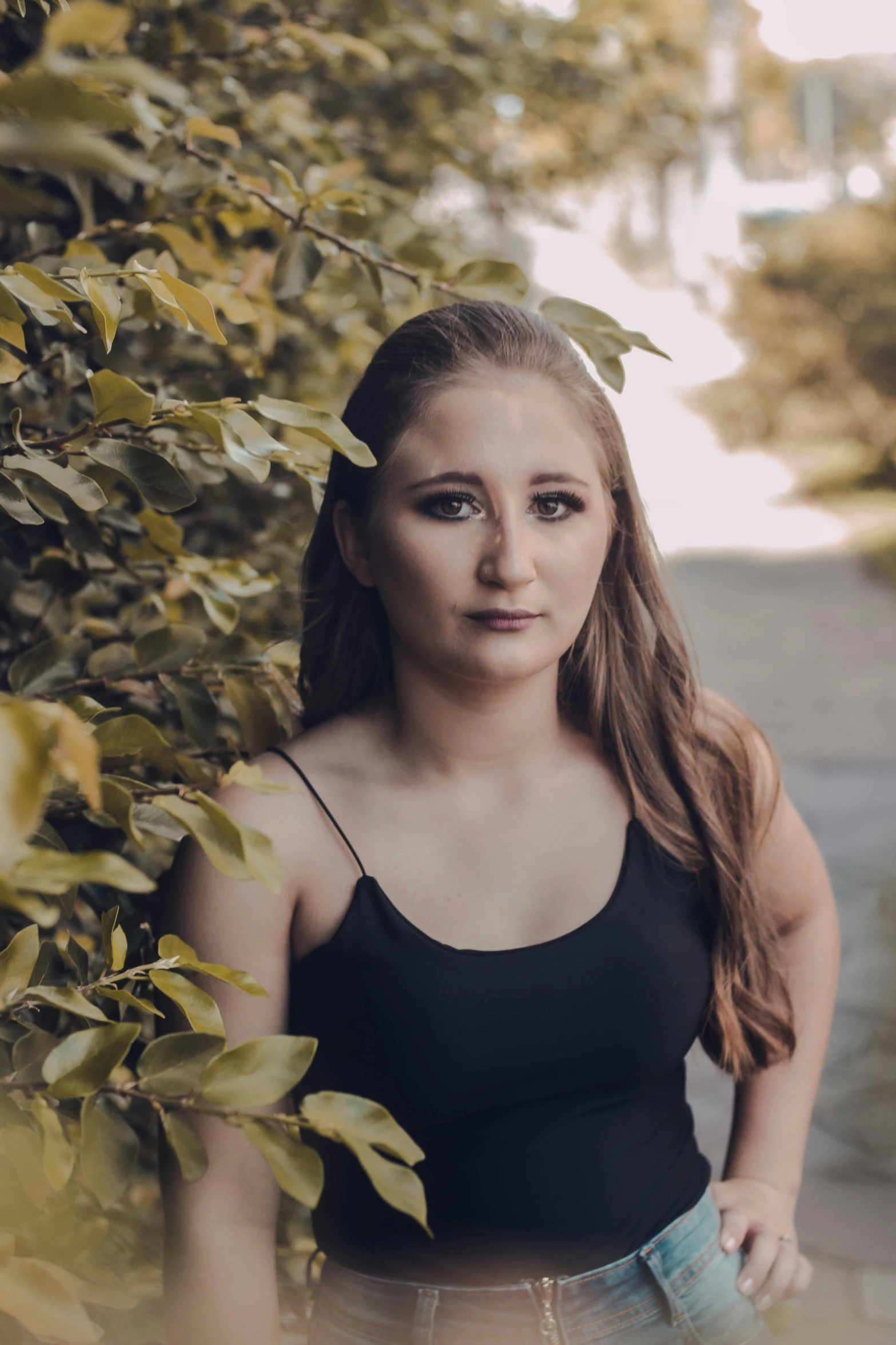 a beautiful young woman standing in front of a bush, an album cover, pexels contest winner, she is wearing a black tank top, serious expression, portrait of sanna marin, 2019 trending photo