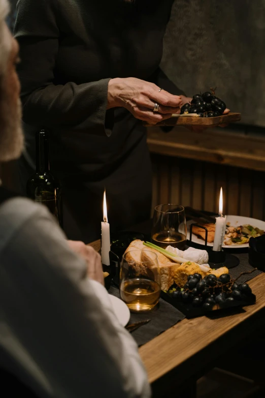 a group of people sitting around a table with food, holding a candle, wine, dark and moody aesthetic, old man