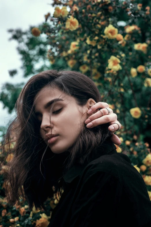 a woman standing in front of a bush of yellow flowers, an album cover, inspired by Elsa Bleda, trending on pexels, madison beer girl portrait, rings, beautiful jewish woman, thoughtful )