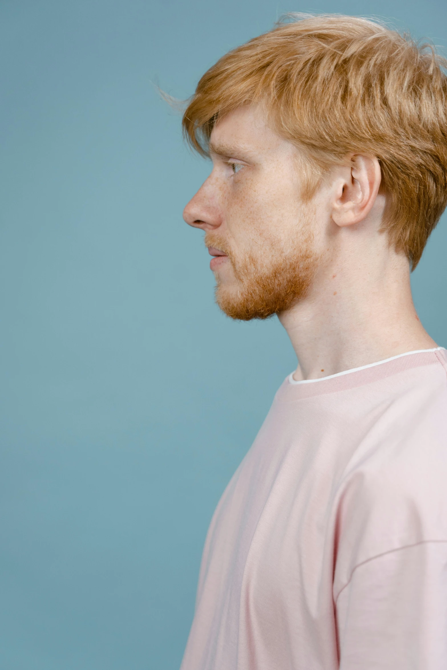 a man standing in front of a blue background, by Lee Gatch, hyperrealism, ginger hair, side profile, pink shirt, ignant