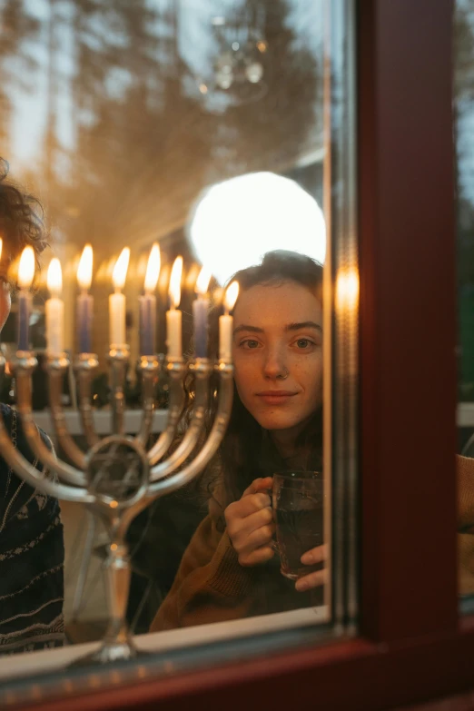 a man and woman looking out a window at a menorah, a portrait, pexels, teenage girl, drinking, a cozy, square