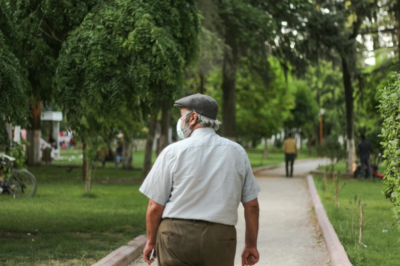 a man walking down a sidewalk while talking on a cell phone, by Ismail Acar, pexels contest winner, realism, in a park, old man doing with mask, green spaces, turkey