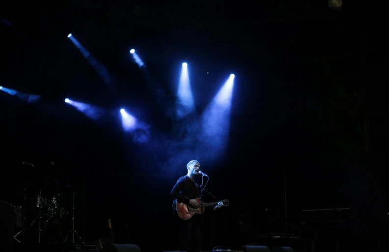 a man that is standing on a stage with a guitar, pexels, it's getting dark, spotlight from face, bright sky, viewed from bellow