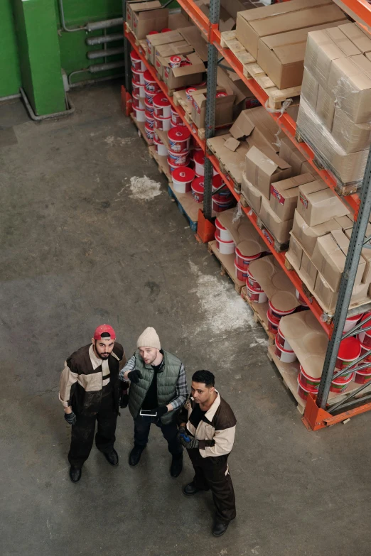 a group of men standing next to each other in a warehouse, pexels contest winner, arbeitsrat für kunst, drone footage, red wings, promotional image, standing on a shelf