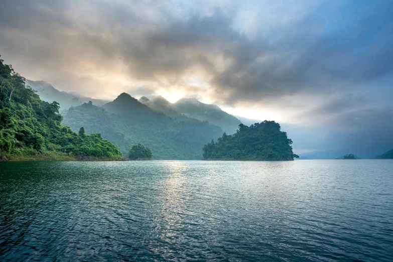 a large body of water surrounded by trees, inspired by Pierre Pellegrini, unsplash contest winner, sumatraism, sun rises between two mountains, vietnam, fjords, conde nast traveler photo