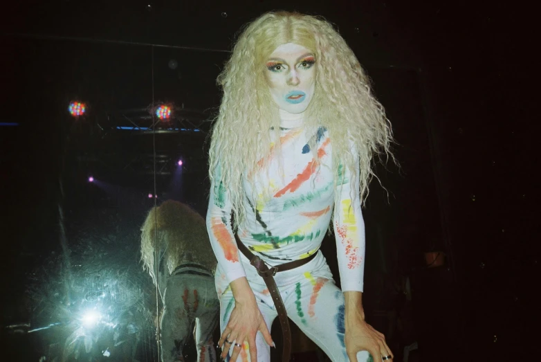 a woman that is standing in front of a mirror, an album cover, inspired by Elsa Bleda, white facepaint, performing on stage, drag, low quality photo