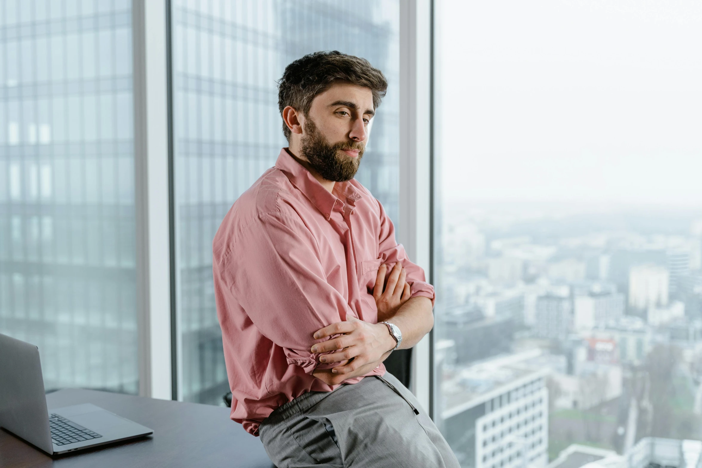 a man sitting on top of a desk next to a laptop, inspired by Nelson Alexander Ross, pexels contest winner, renaissance, looking off to the side, looking over city, daniel radcliffe, office clothes