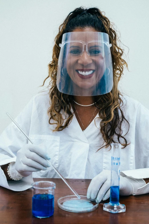 a woman sitting at a table with a face shield on her head, pexels contest winner, renaissance, with a lab coat, big smile white teeth, dna experiment, hispanic