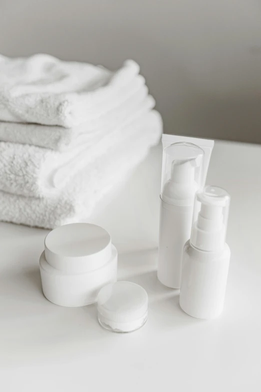 a pile of white towels sitting on top of a table, skincare, thumbnail, bottle, white room