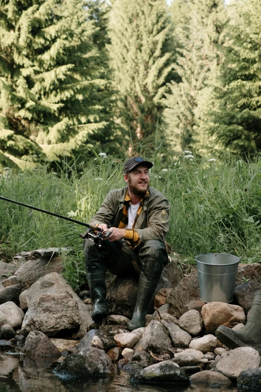 a man sitting on a rock next to a body of water, fishing pole, mr beast, full body length, trout in pants