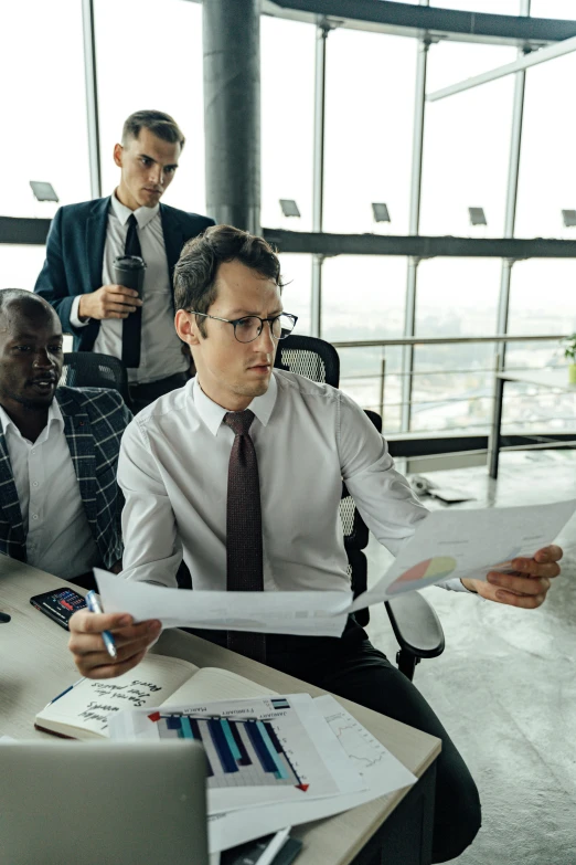 a group of men sitting around a table with papers, pexels contest winner, highrise business district, man with glasses, thumbnail, non-binary