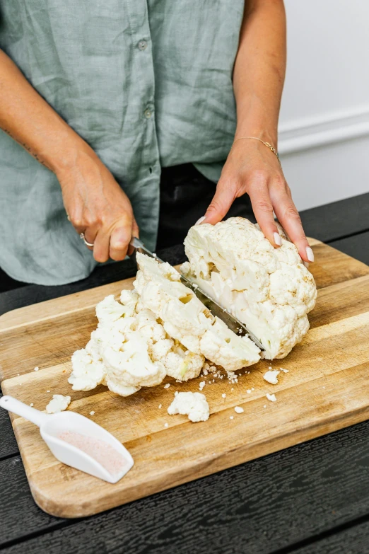 a woman cutting a piece of cauliflower on a cutting board, enormous hands, perfectly poised, creamy, handcrafted