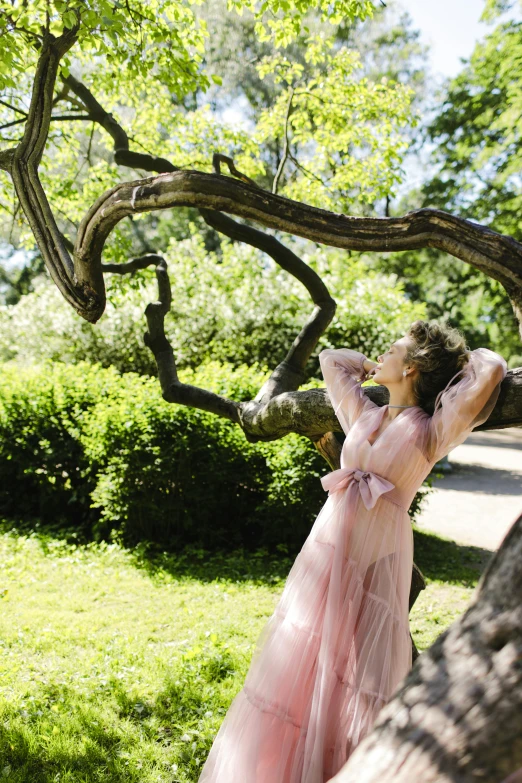 a woman in a pink dress standing next to a tree, inspired by Konstantin Somov, pexels contest winner, romanticism, arms stretched out, francesca woodman style, parks and gardens, wearing organza gown