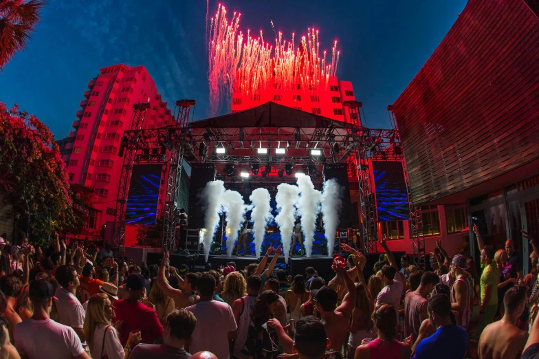 a group of people standing on top of a stage, pyrotechnics, night on a summer miami beach, red and blue neon, block party