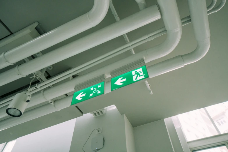 a green exit sign mounted to the ceiling of a building, a cartoon, pexels, happening, pipes, instagram post, medical lighting, on ship