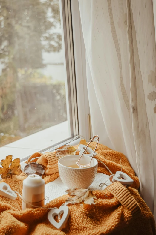 a table topped with a bowl of food next to a window, a still life, trending on pexels, fine art, hot cocoa drink, orange yellow ethereal, spa, autum